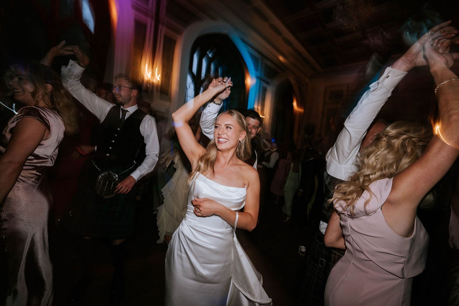 Wedding guests dancing energetically at a dimly lit reception party.