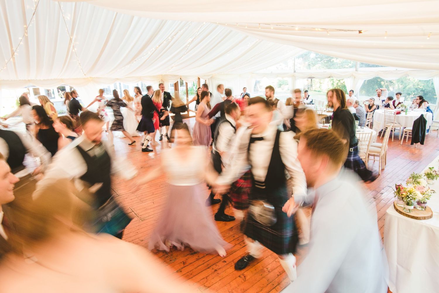 Motion-blurred dancers twirling and moving across a dance floor at an indoor celebration.