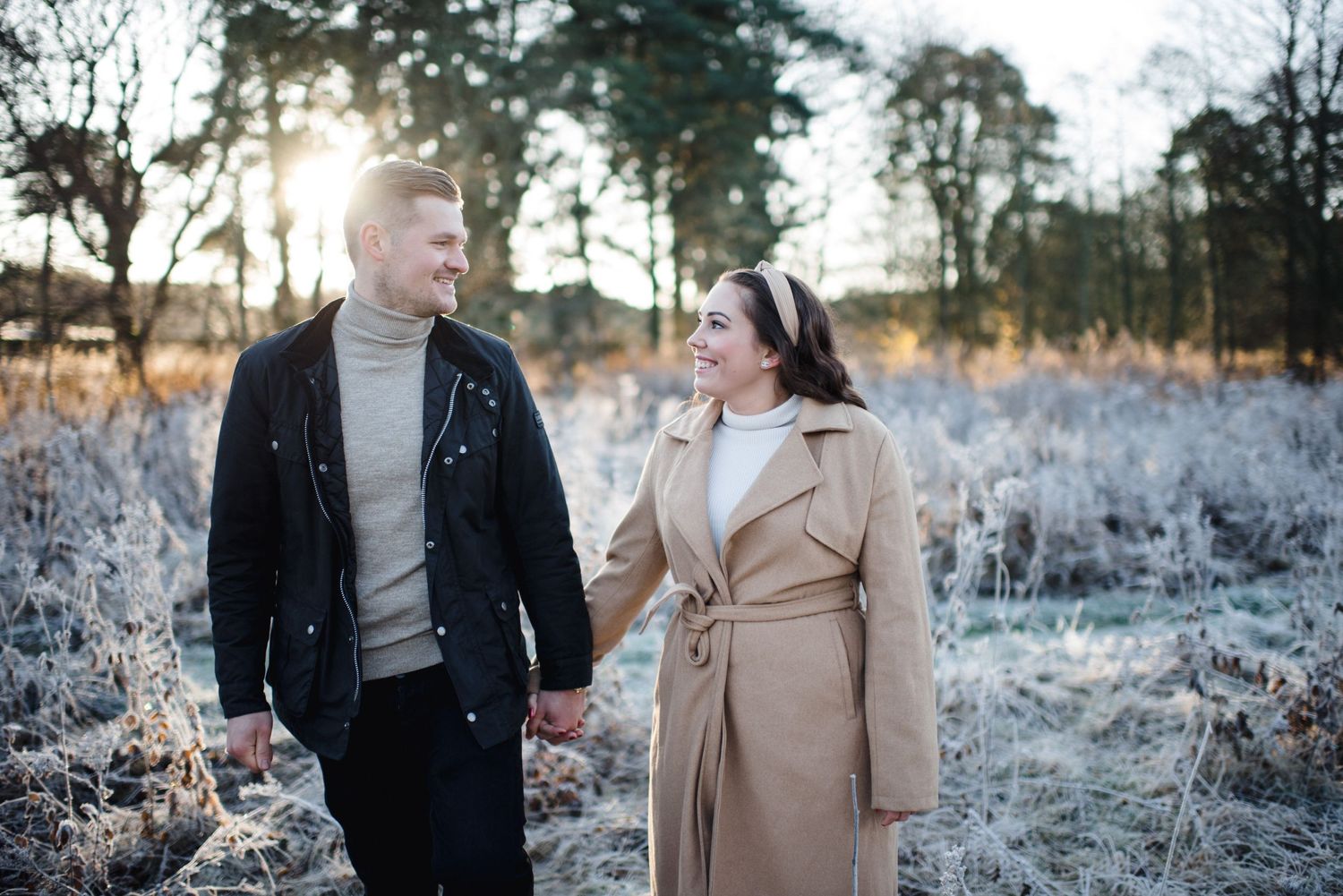 A couple walks hand in hand through a frost-covered winter landscape.