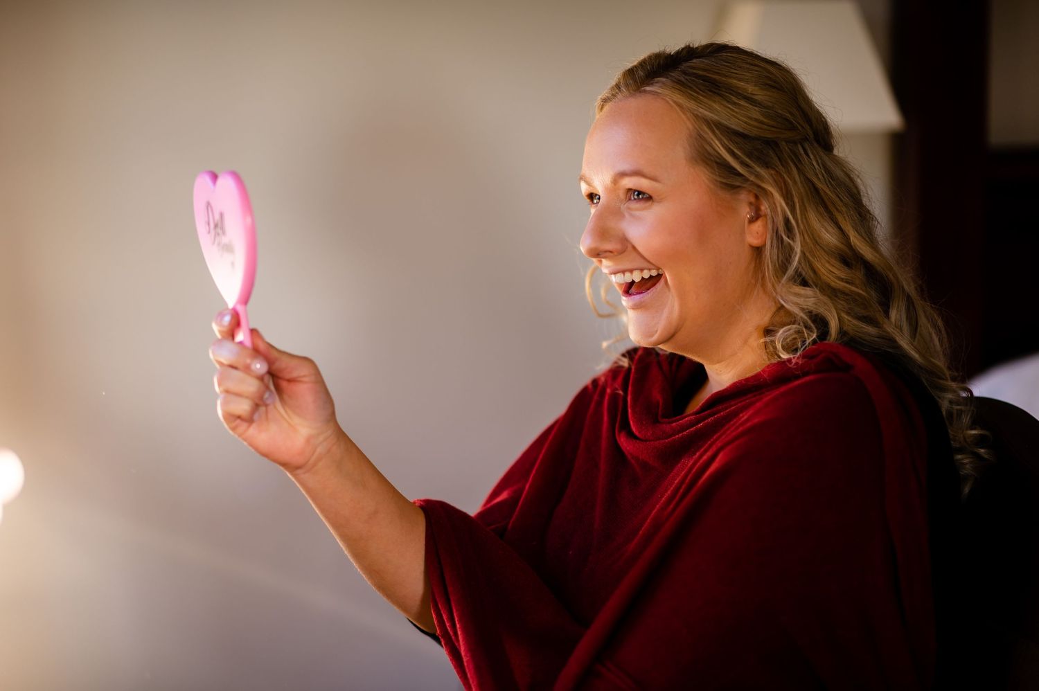 Person in red sweater laughing while holding a pink light stick in a dimly lit setting.