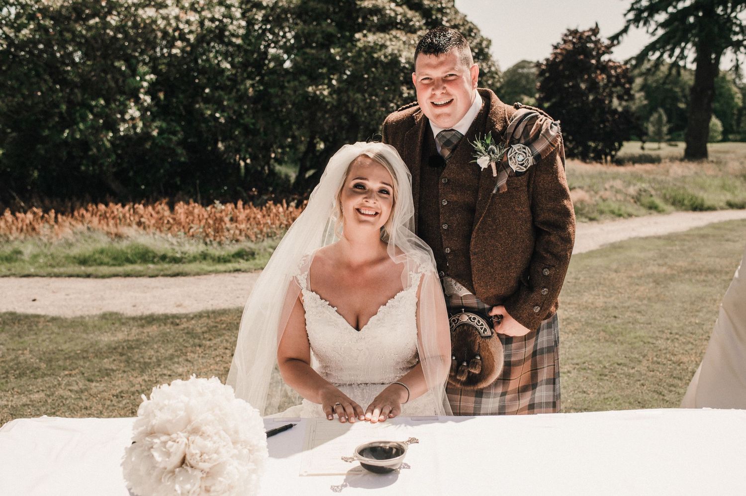 A joyful moment at an outdoor wedding signing table with Scottish Highland attire.