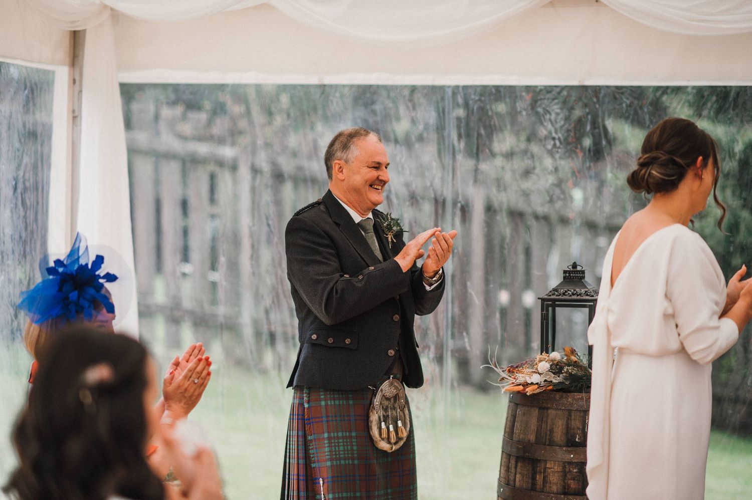 Wedding guest in traditional Scottish kilt applauding during ceremony.
