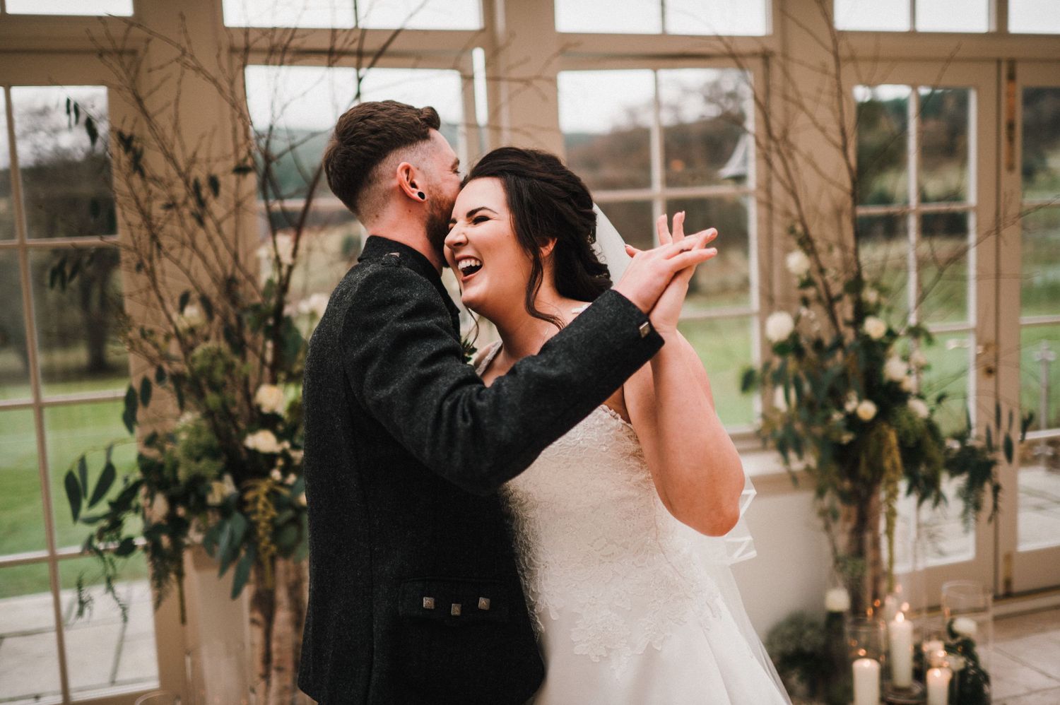 Wedding couple shares intimate moment during celebration in glass-walled venue.