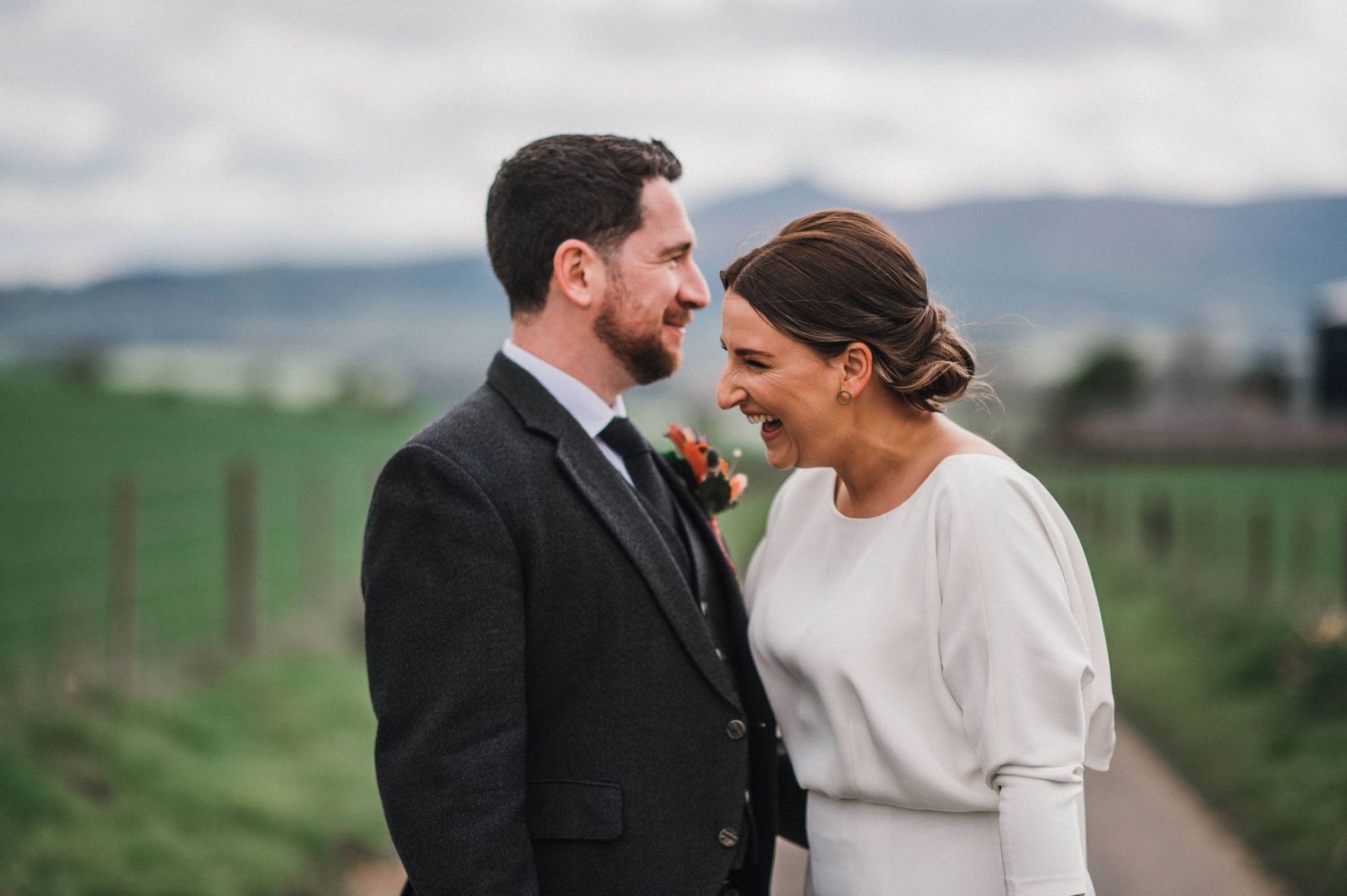 A tender moment between newlyweds sharing laughter in a rural countryside setting.