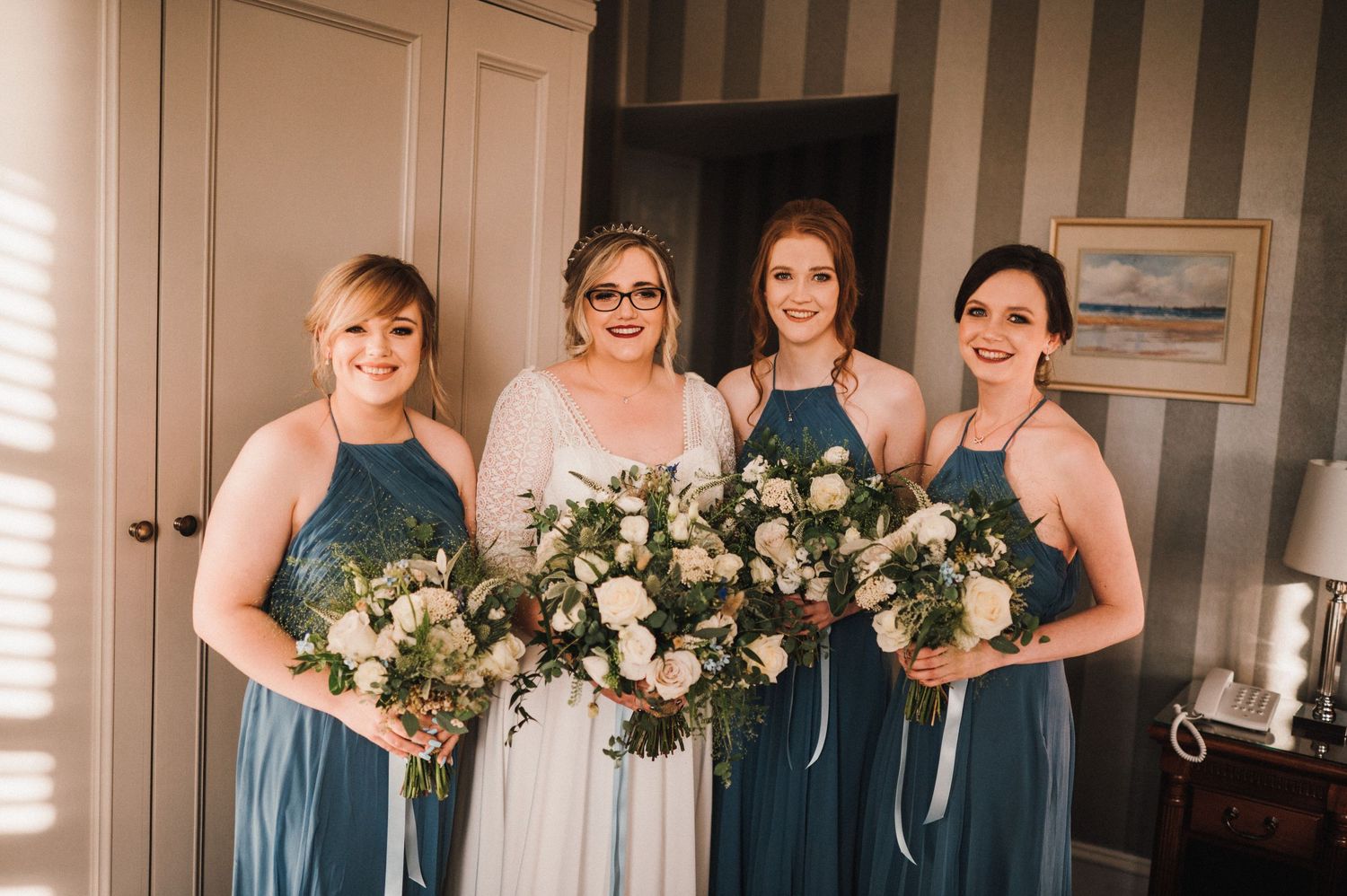 Wedding party with bridesmaids in teal dresses holding elegant white and pink floral bouquets.