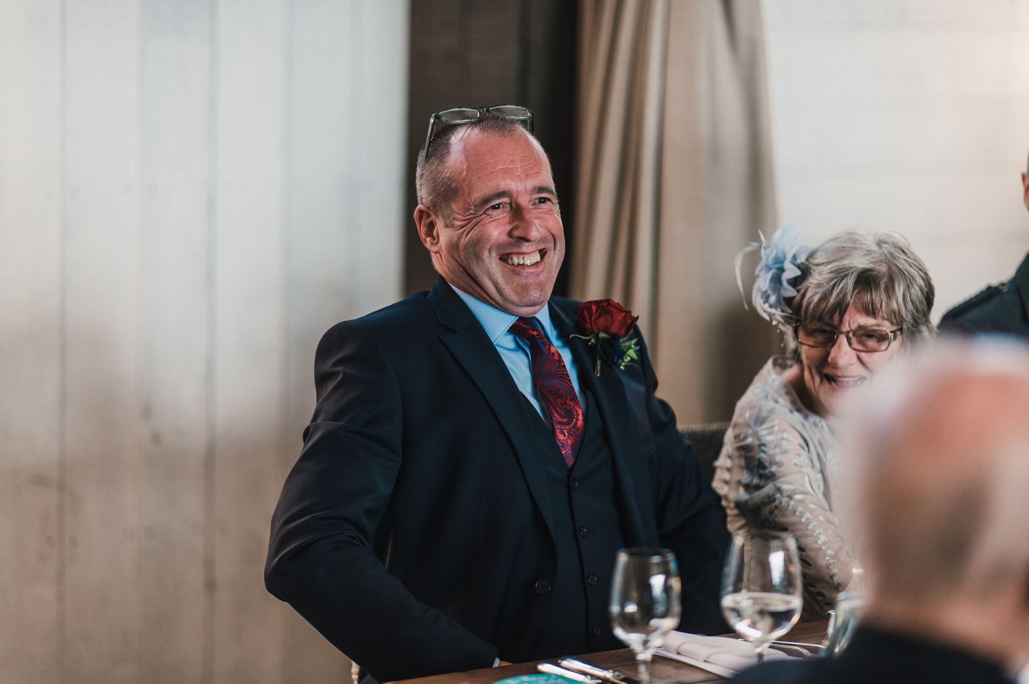 A guest at a formal event smiles while seated at a decorated dining table.