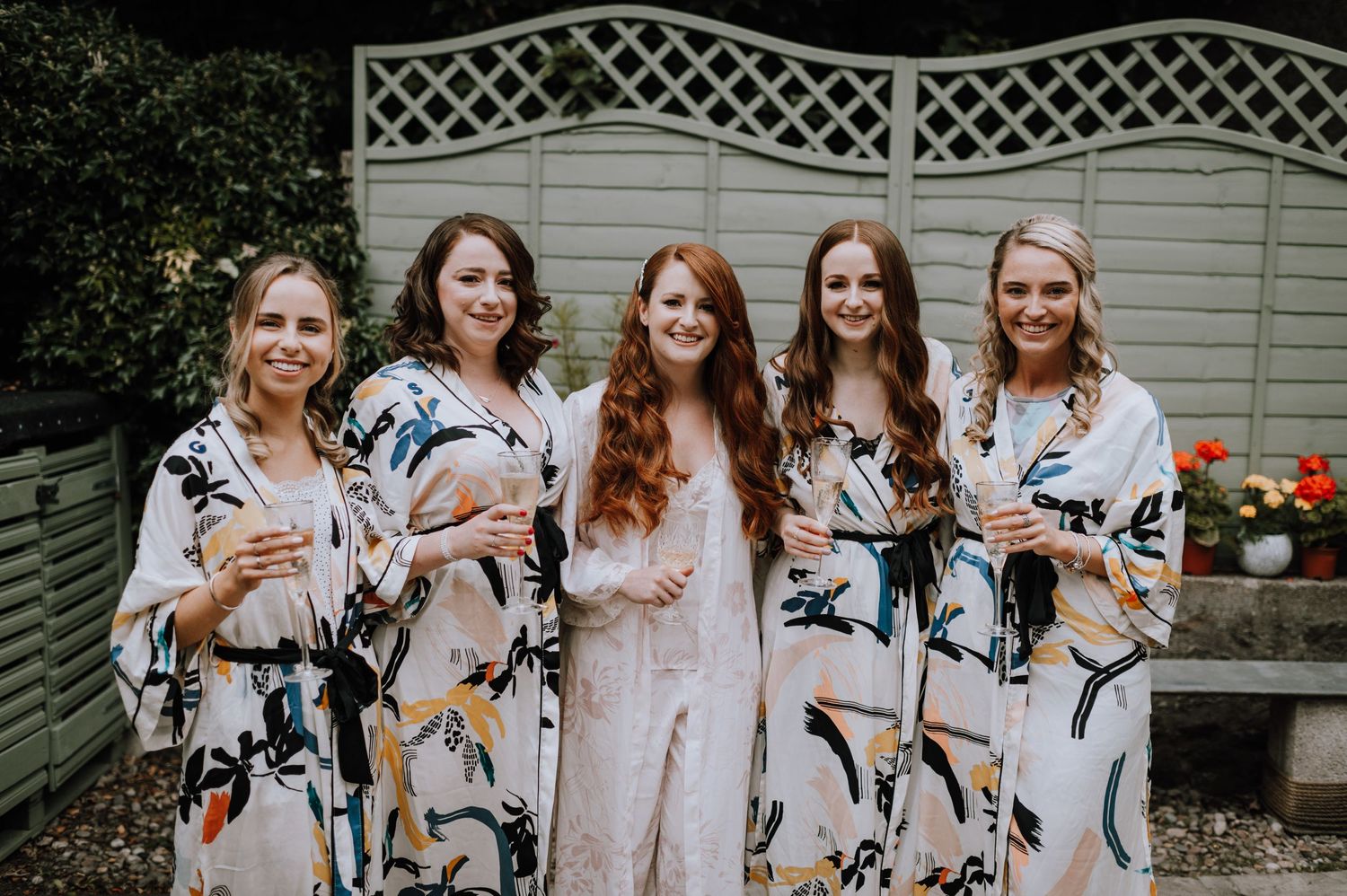 Group wearing matching floral robes gather in front of a white garden fence.