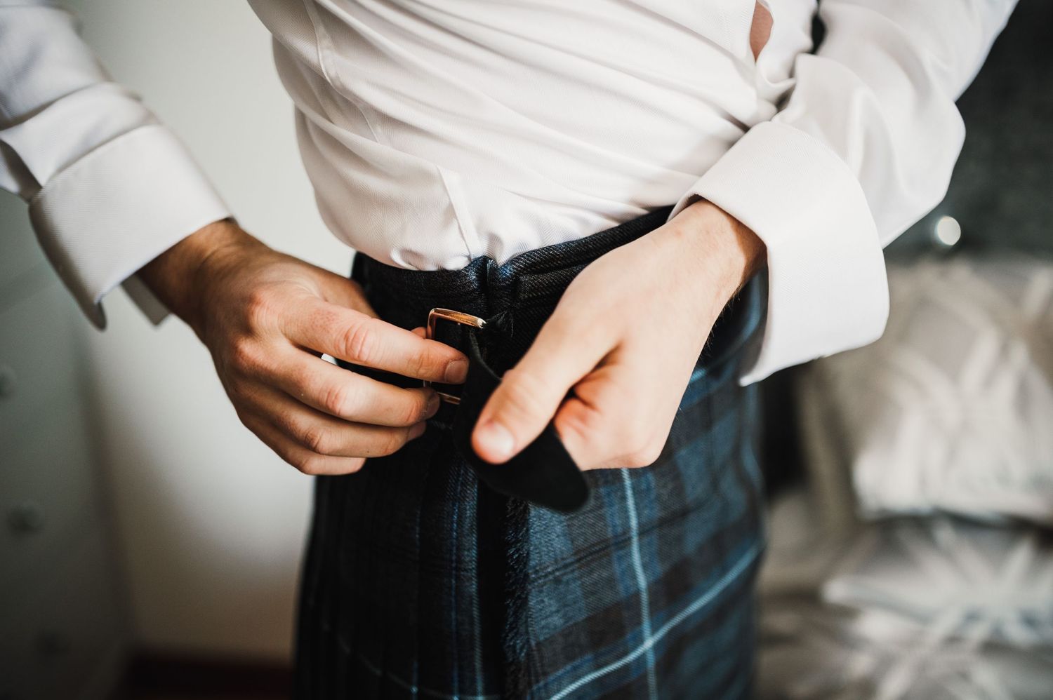 Close up of hands fastening a blue plaid kilt.