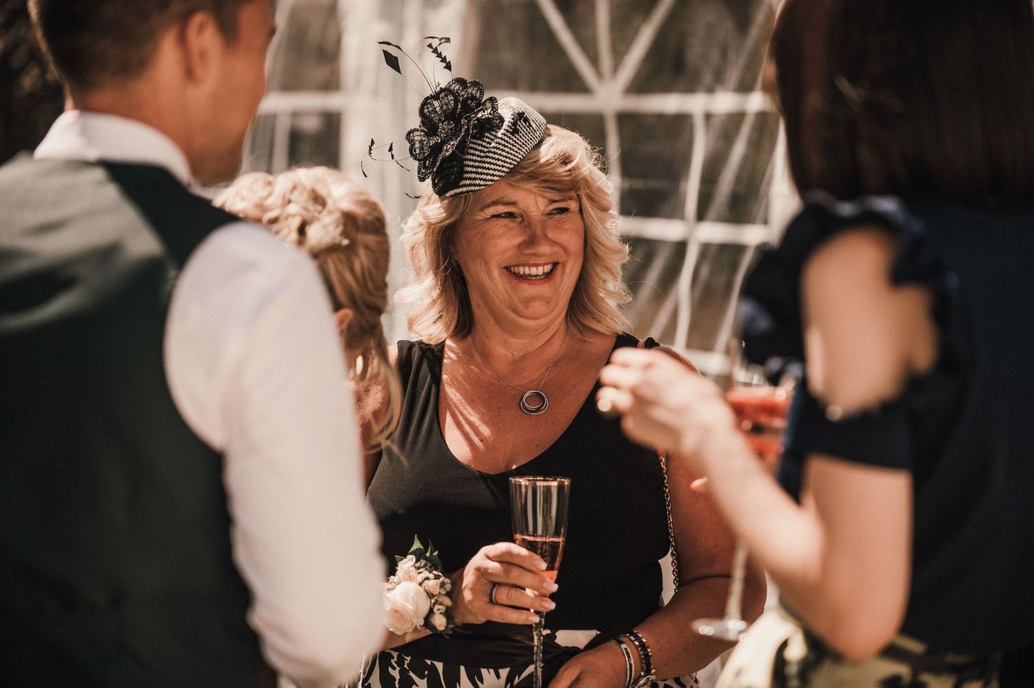Wedding guests enjoying drinks and laughter at an outdoor tent reception.