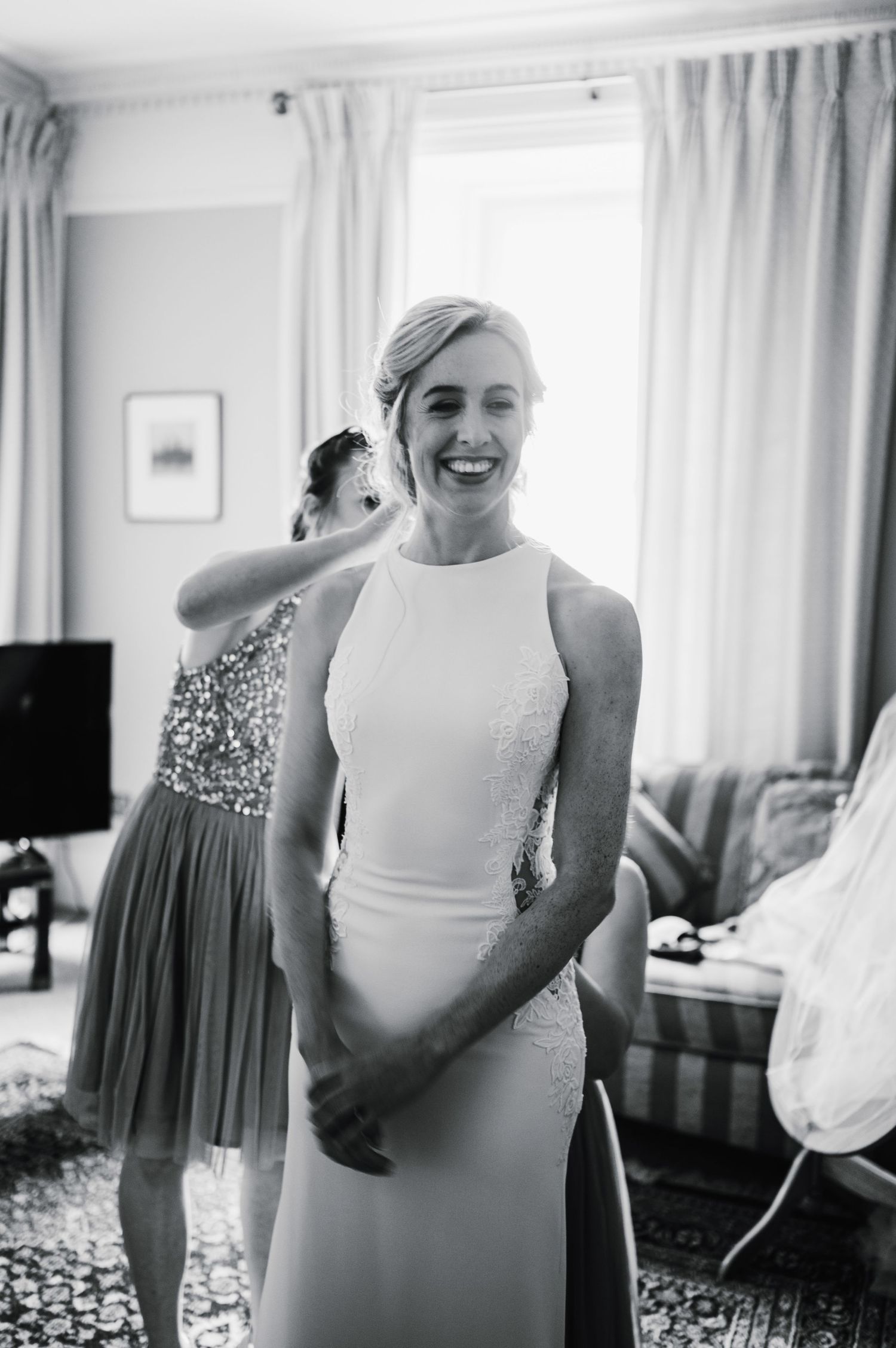 A black and white photo of someone in a sleek white wedding dress smiling joyfully.