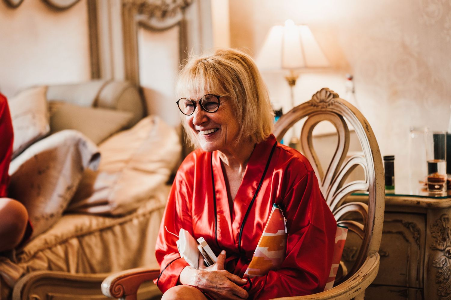 Candid moment in red robe while relaxing in ornate chair during wedding preparations.