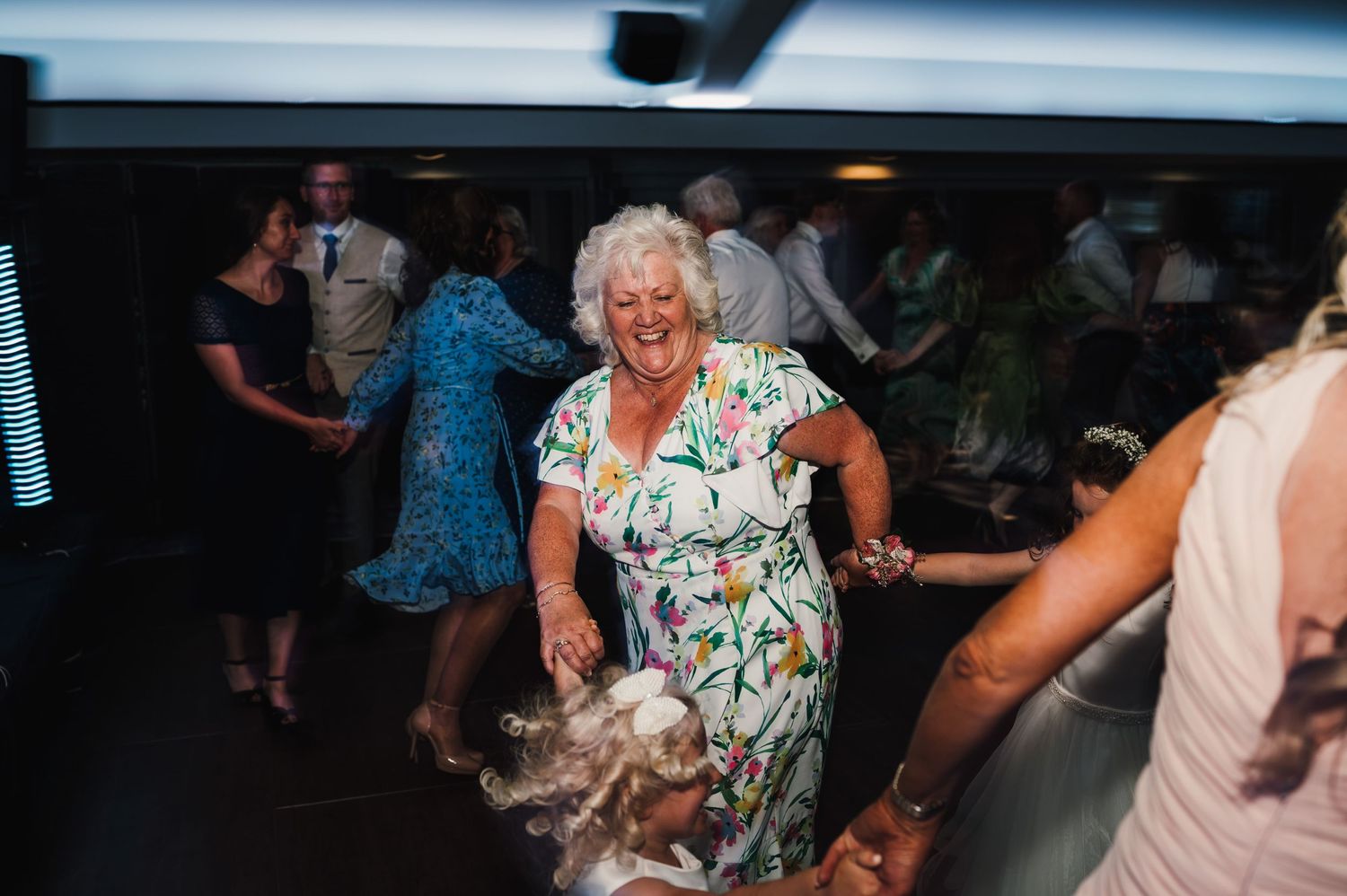 An energetic dancer in a floral dress enjoying the dance floor at a wedding reception.