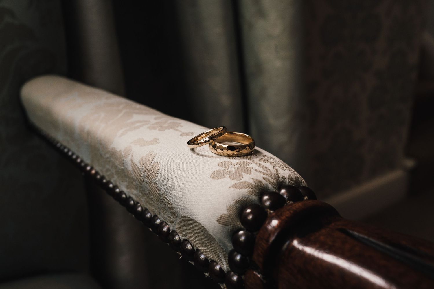 Wedding rings rest on a cream-colored cushioned surface in dramatic lighting.