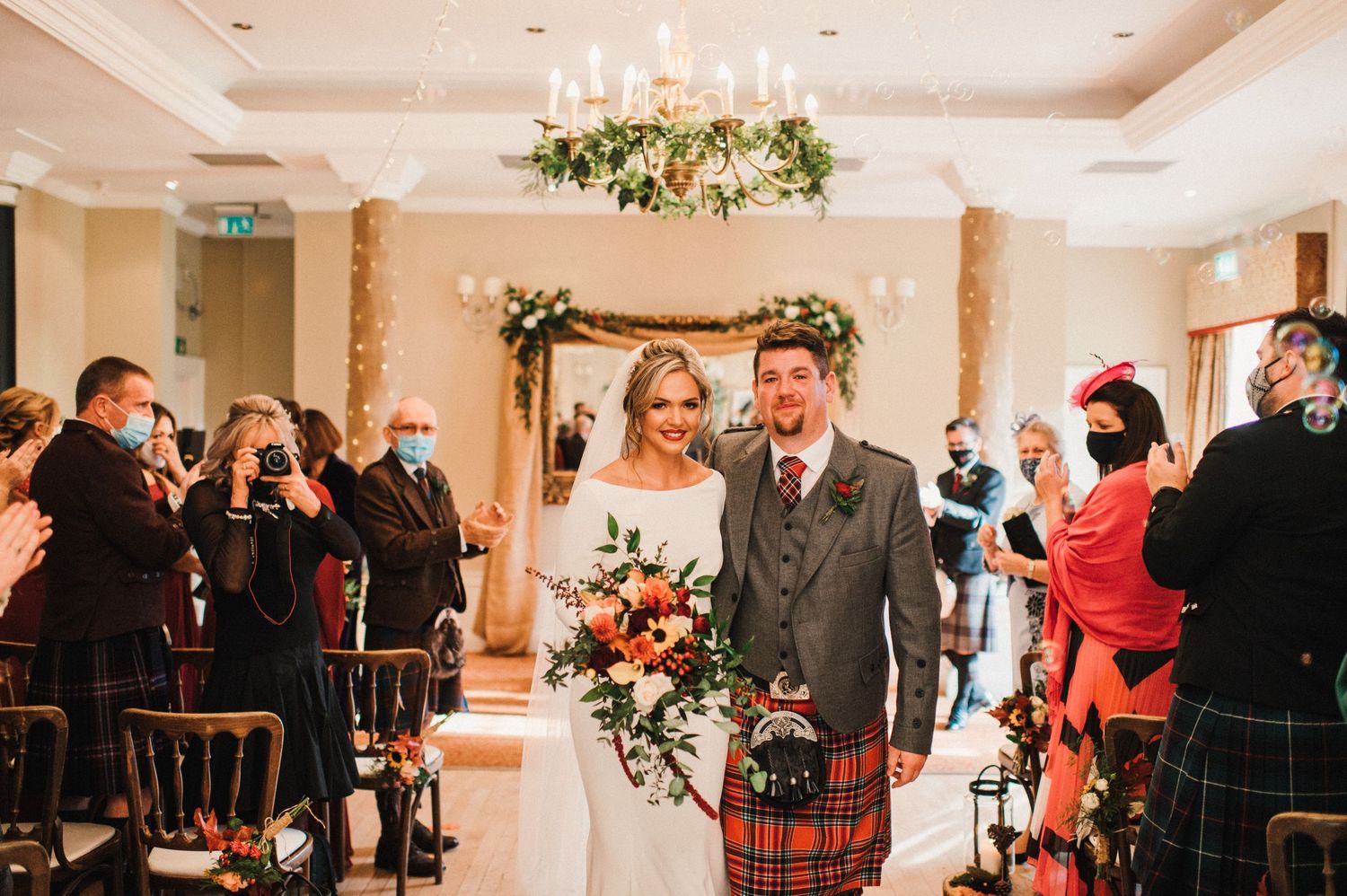 Wedding ceremony in elegant venue with Scottish kilts and floral arch decorations.