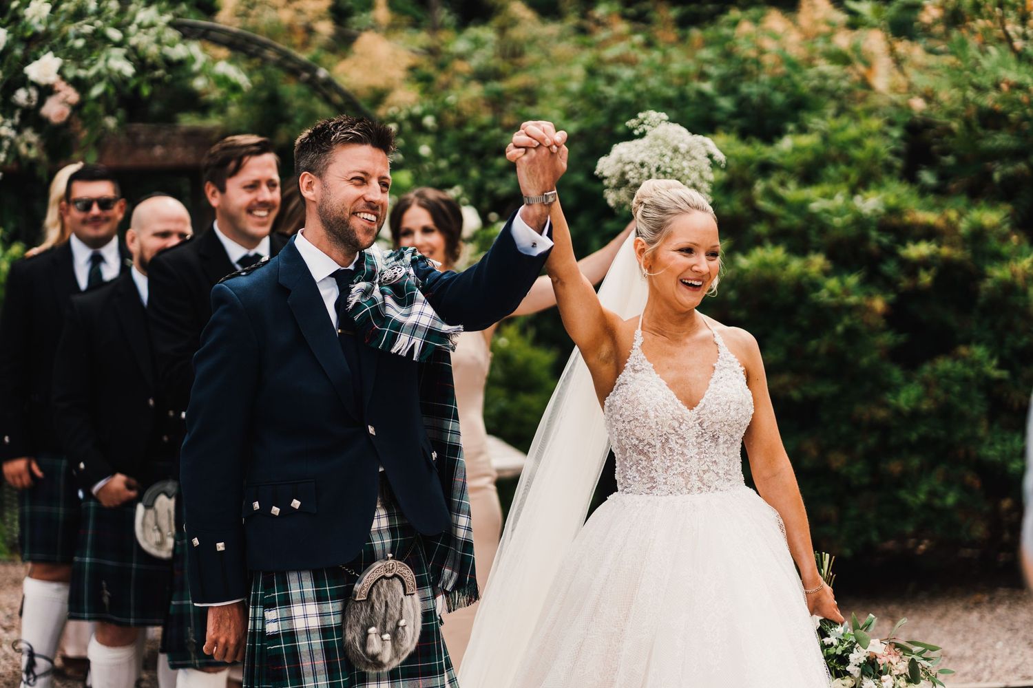 A wedding celebration on garden grounds with the wedding party wearing traditional Scottish kilts.