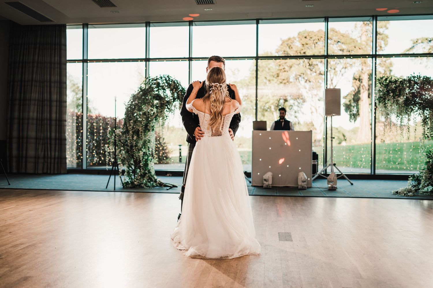 First dance moment in a bright reception venue with floor-to-ceiling windows and hanging greenery.
