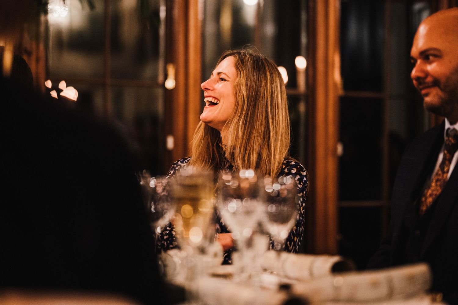 Guest laughing joyfully during elegant candlelit dinner reception.