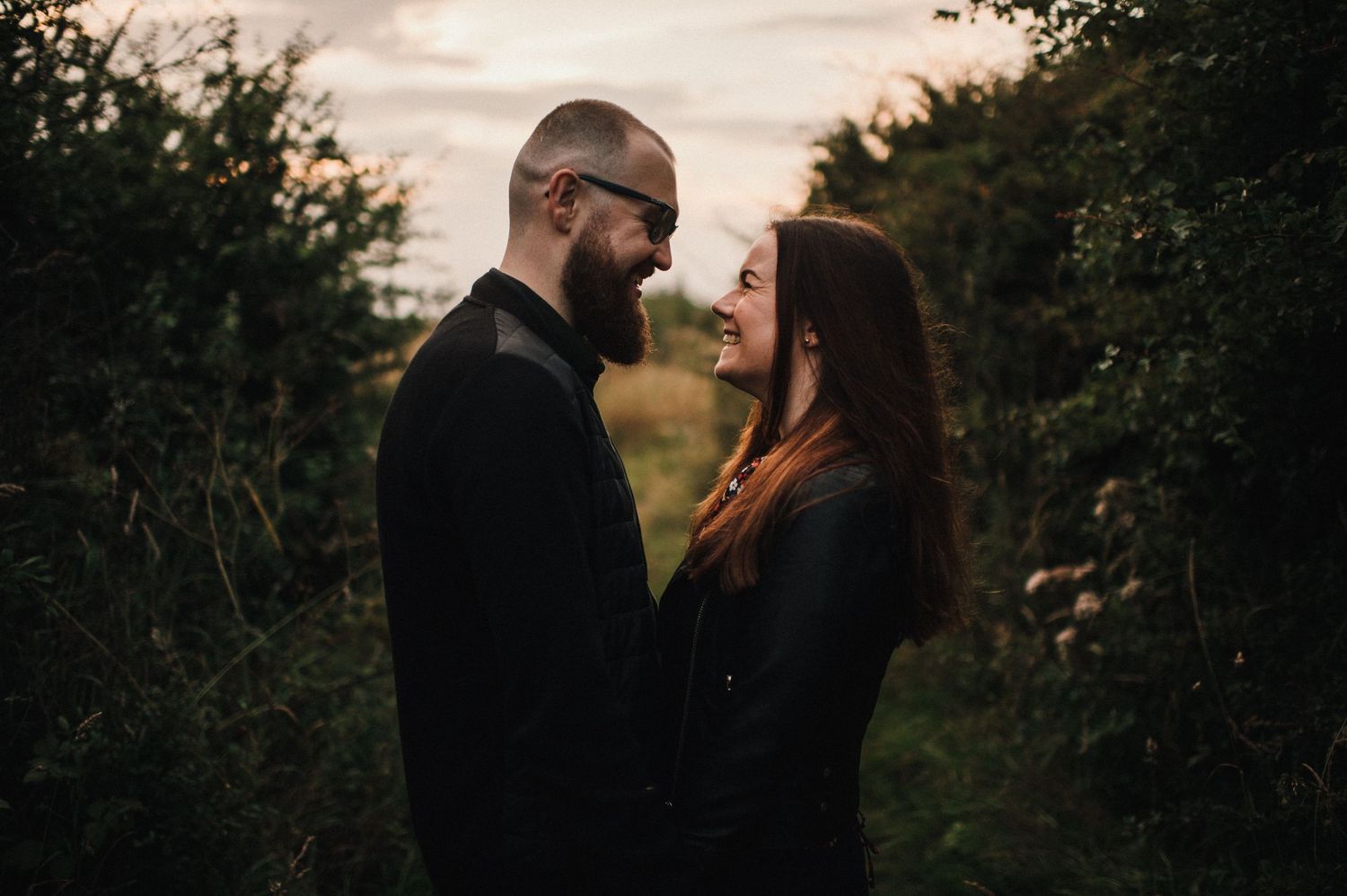 A couple shares an intimate moment against a dusky natural backdrop with trees.