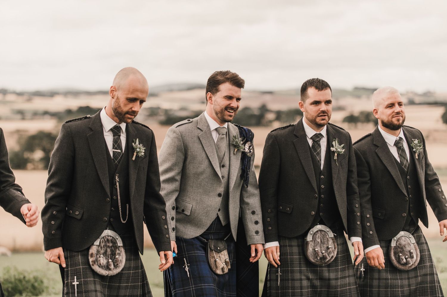 Group of men in formal Scottish attire with kilts standing together outdoors.