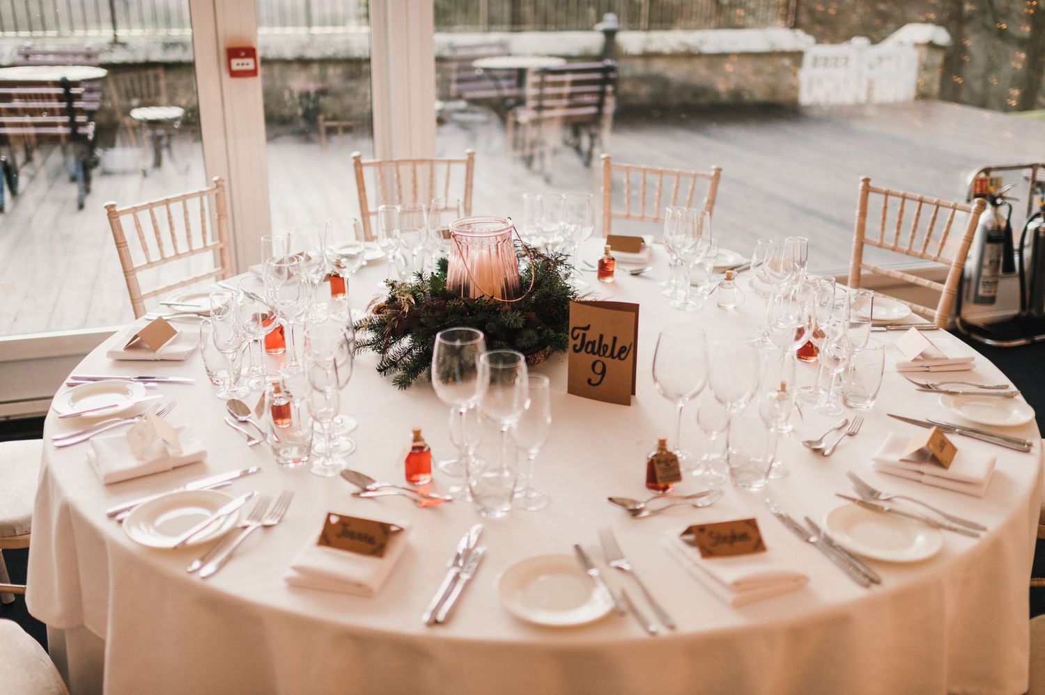 An elegant round wedding reception table with place settings, centerpiece and chiavari chairs.