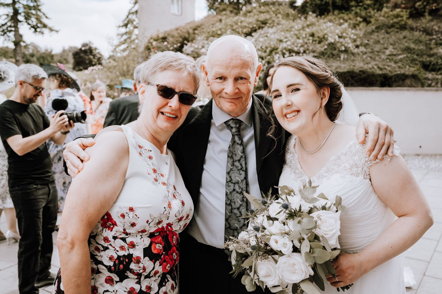 Wedding party poses with bouquets outside during celebration.