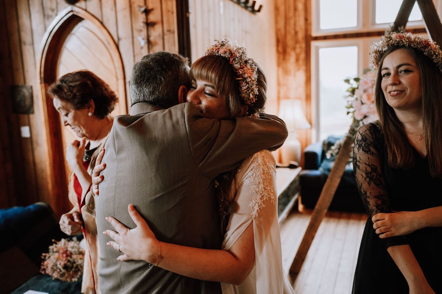 Joyful hugs exchanged during wedding celebrations in a wood-paneled room with decorative flowers.