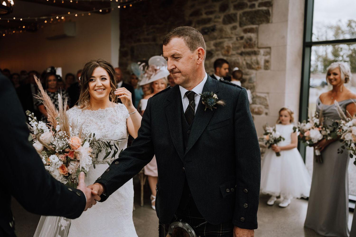 Indoor wedding ceremony in rustic venue with stone walls and elegant floral arrangements.