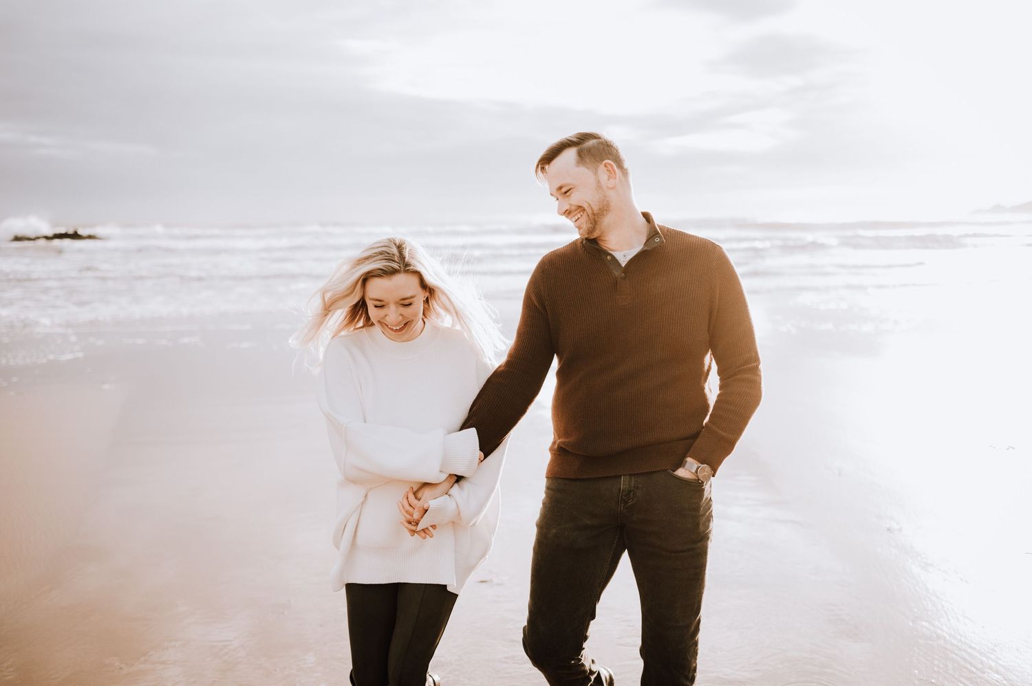 A couple shares a joyful moment while walking together on a sandy beach.
