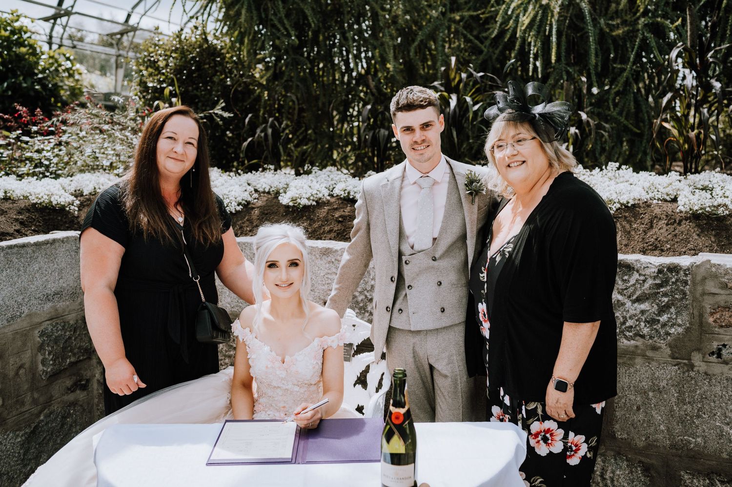 Wedding party gathers at a signing table in a greenhouse with lush greenery.