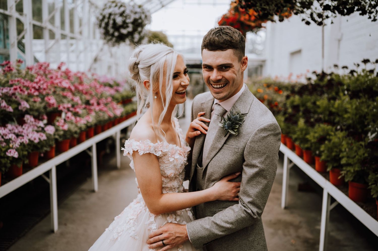 Candid wedding moment in a greenhouse walkway surrounded by colorful flowers.