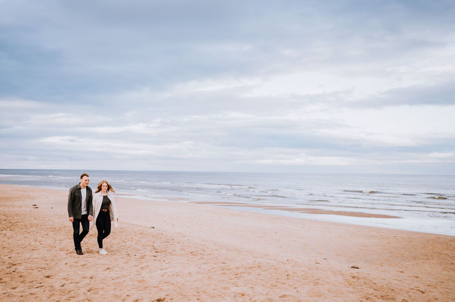 Silhouetted couple walking along shoreline on a cloudy beach day.