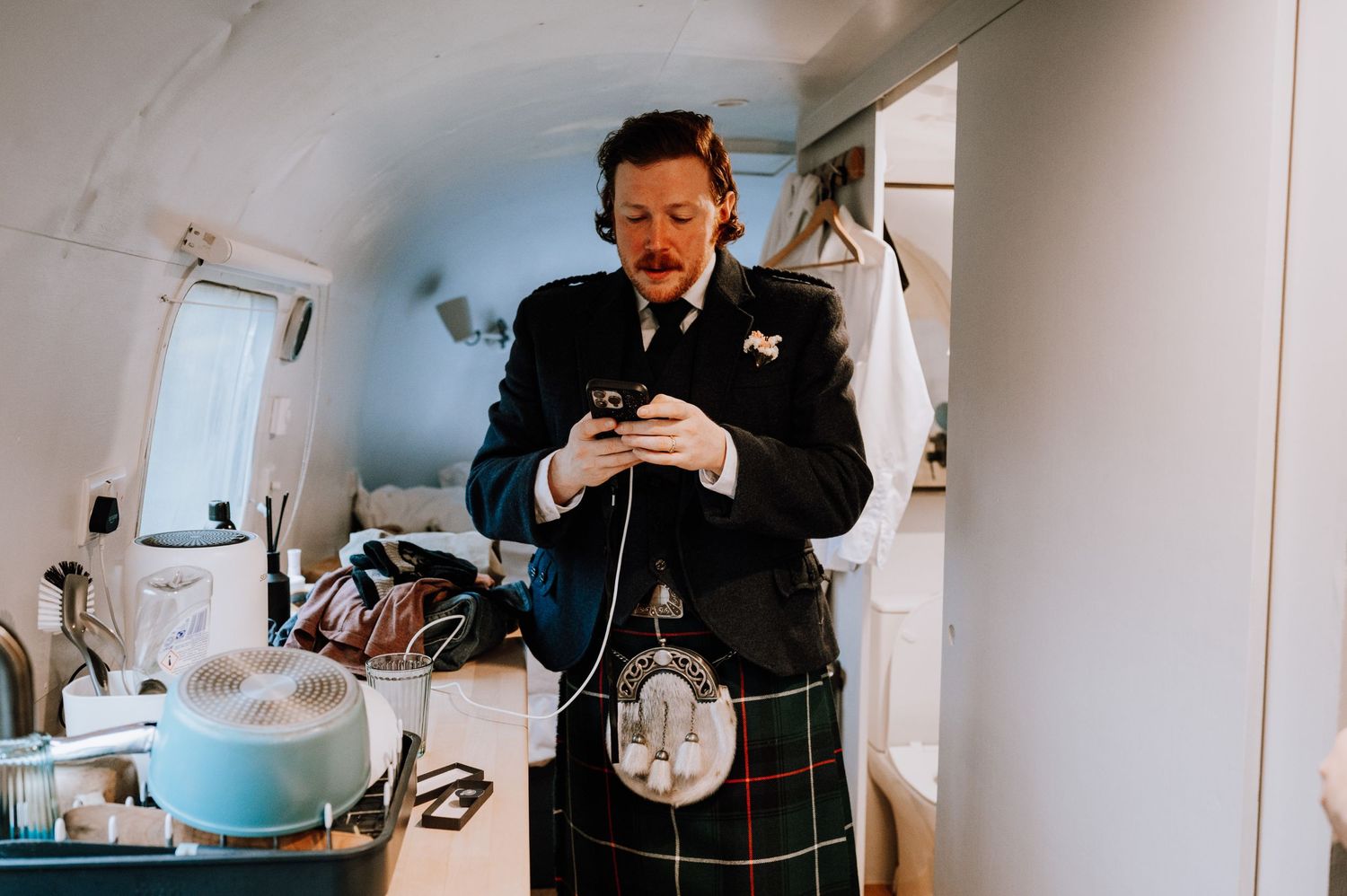 Person in traditional kilt checking phone while standing in mobile changing area.