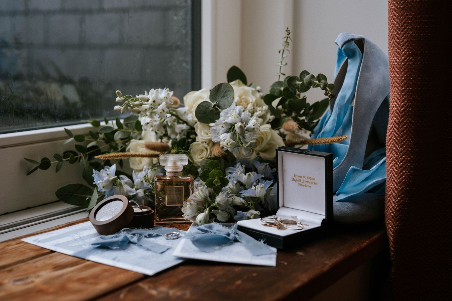 Wedding details including flowers, perfume, and stationery arranged on a wooden windowsill.