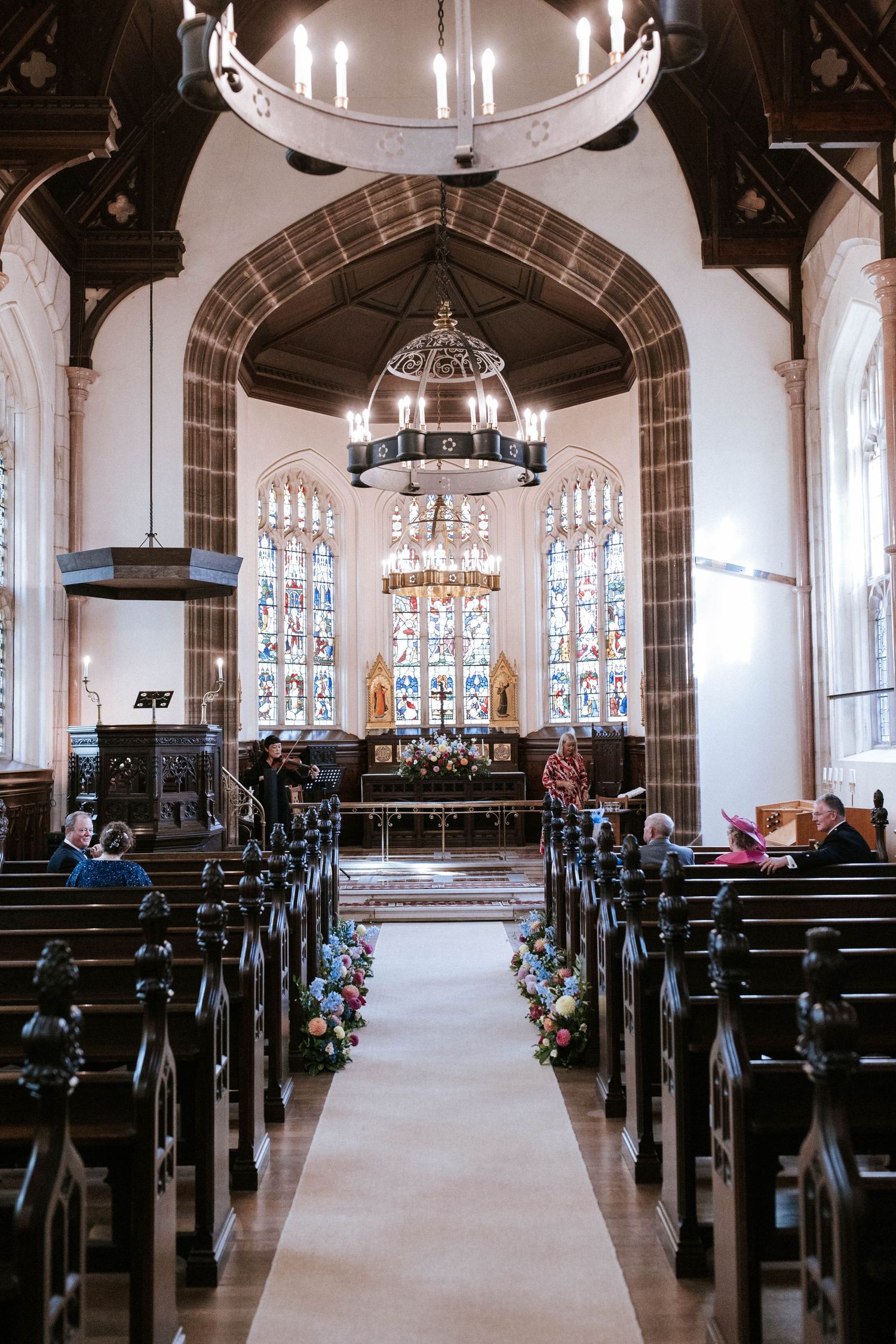 Church sanctuary with rows of dark wooden pews and stained glass windows illuminated by natural light.