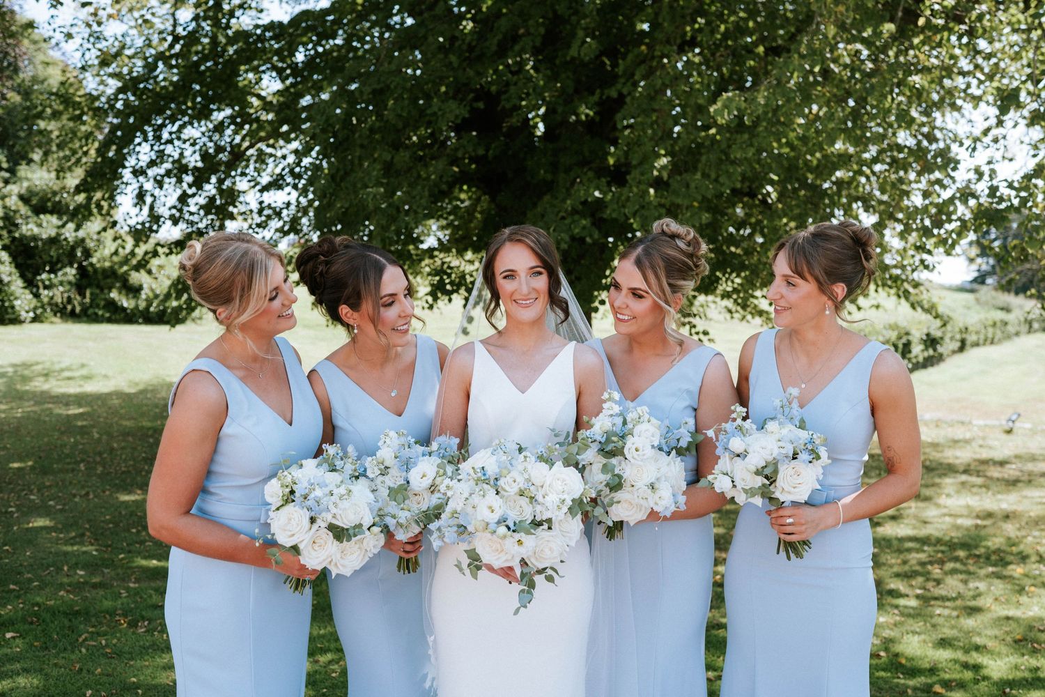 Aberdeen Wedding Photography. Bridesmaids in light blue dresses hold white floral bouquets while standing outdoors.