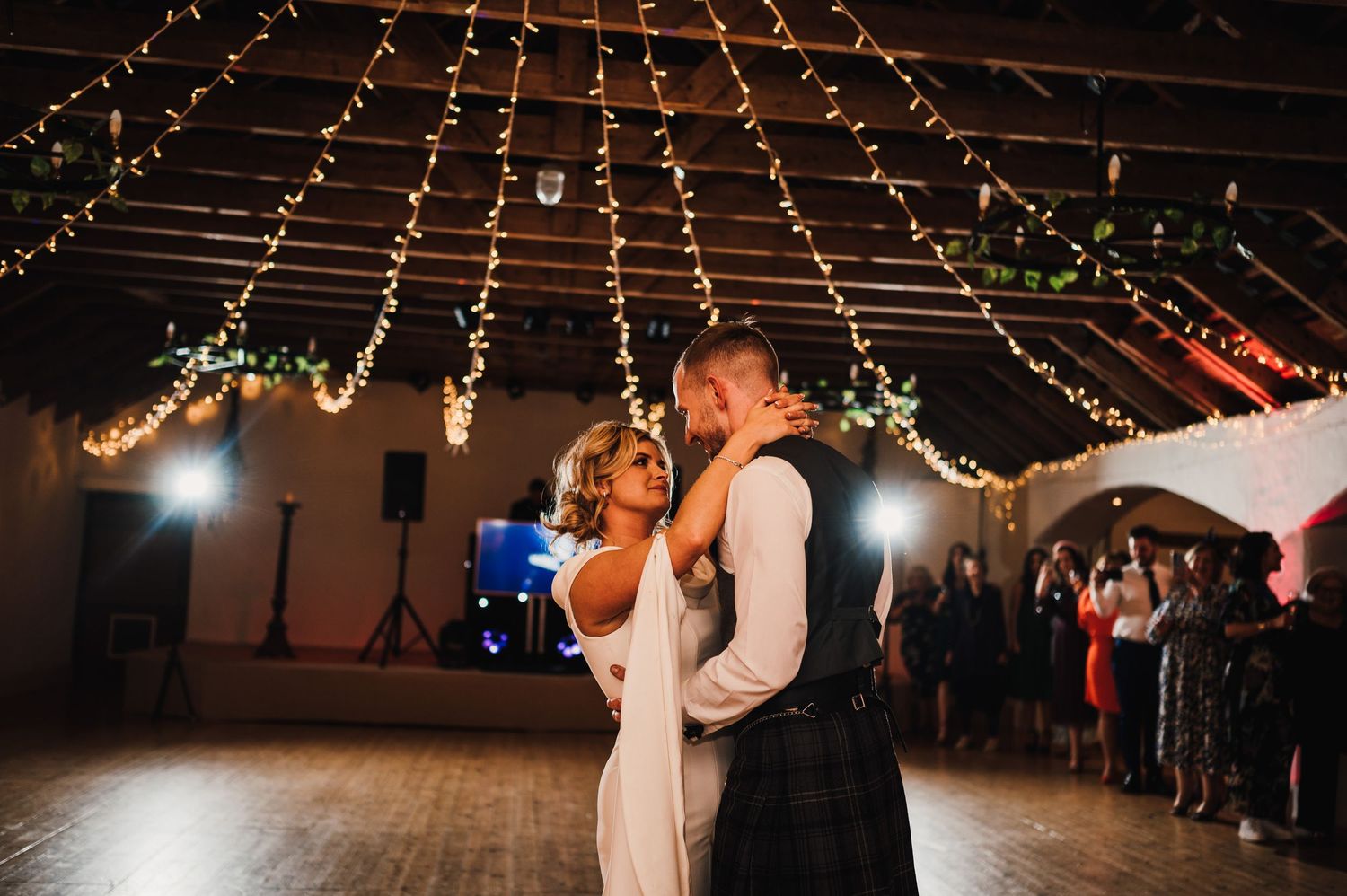 Wedding reception dance floor with string lights hanging from wooden beams creating a romantic atmosphere.