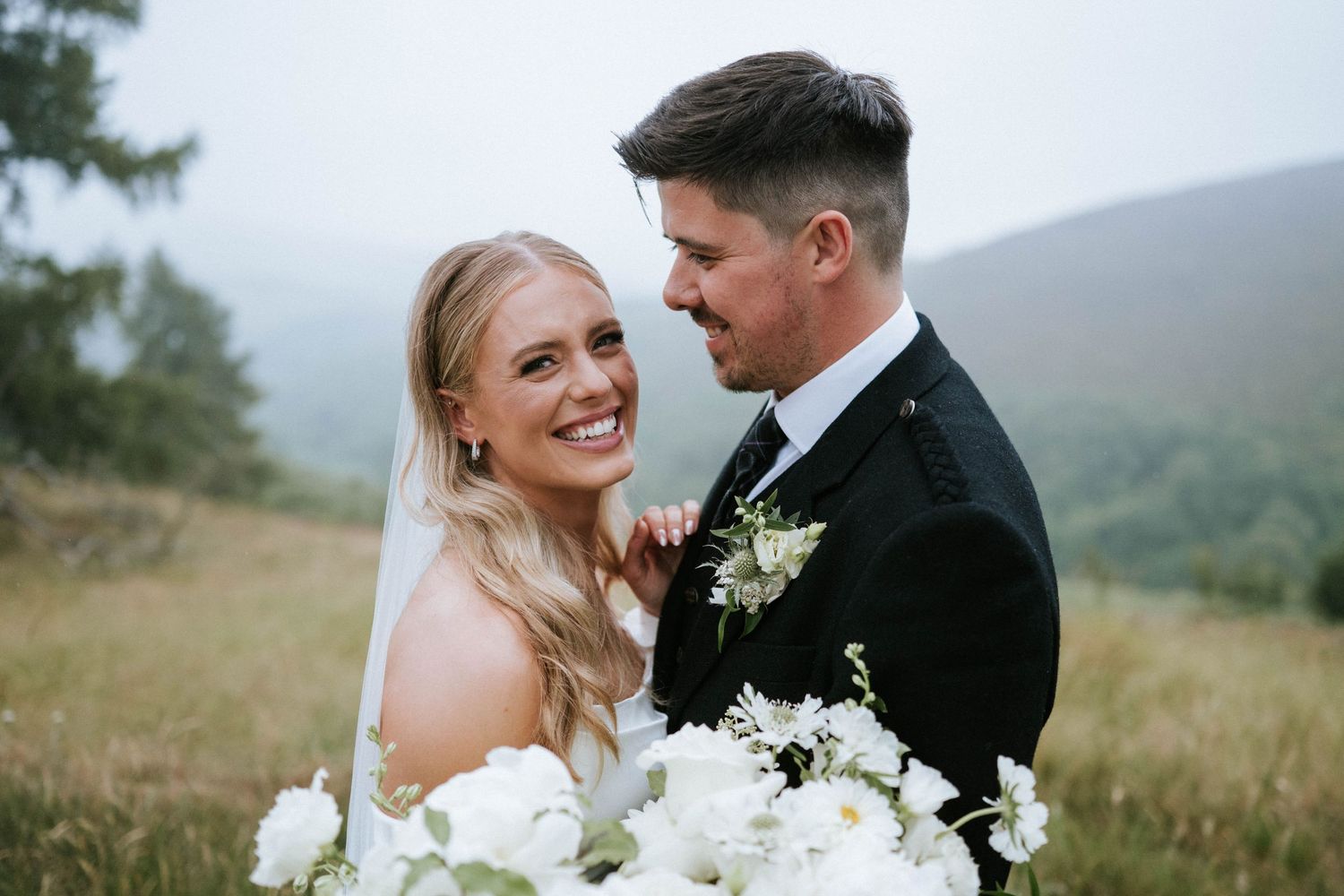 Romantic wedding couple poses in a misty outdoor field during golden hour.