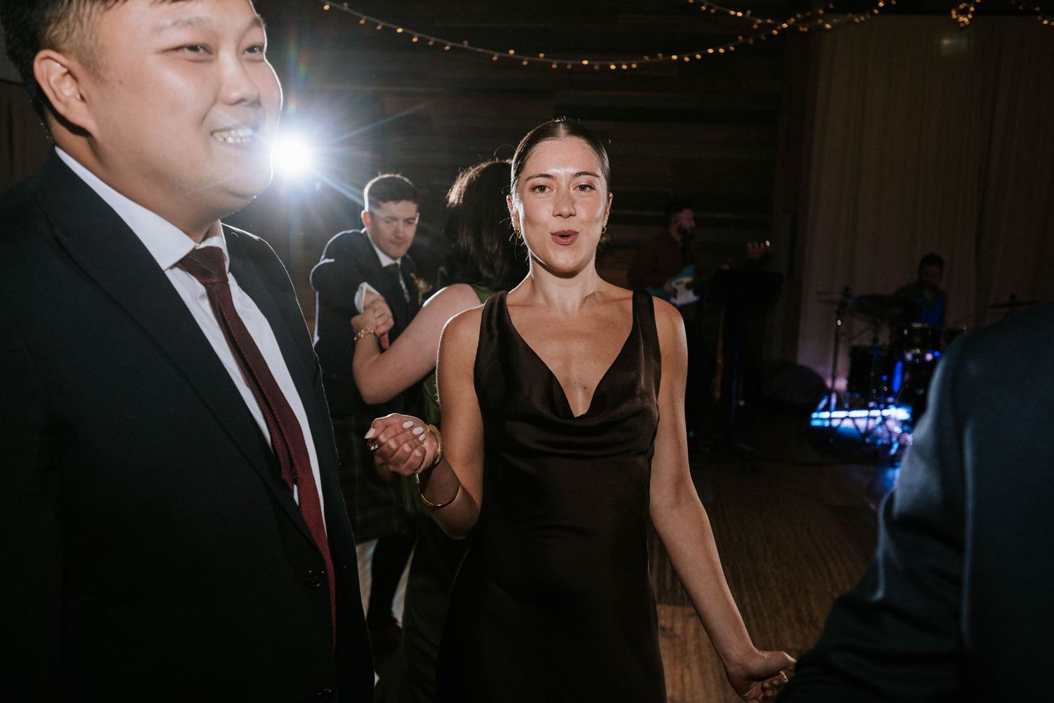 Wedding reception guests dancing in a dimly lit venue with string lights overhead.