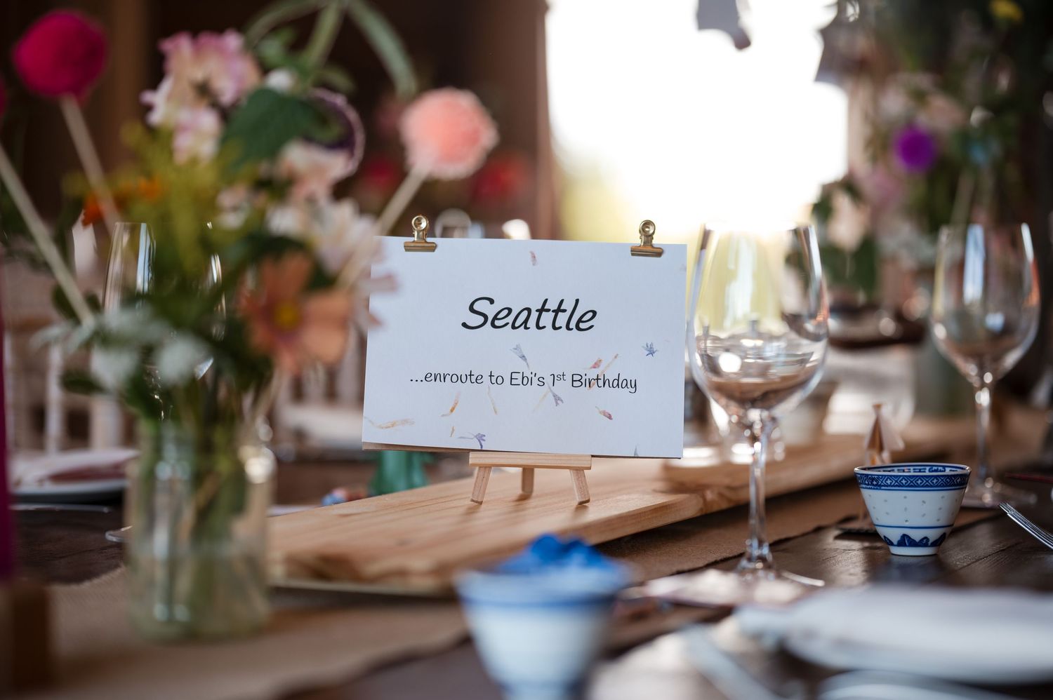 Wedding reception table settings with pink floral centerpieces, wine glasses, and place cards in an elegant indoor venue.