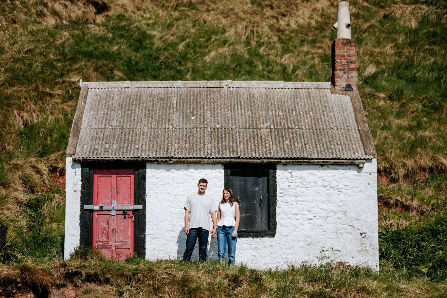 Engagement photography session Aberdeen. A traditional white cottage with red door sits nestled in green rolling hills.