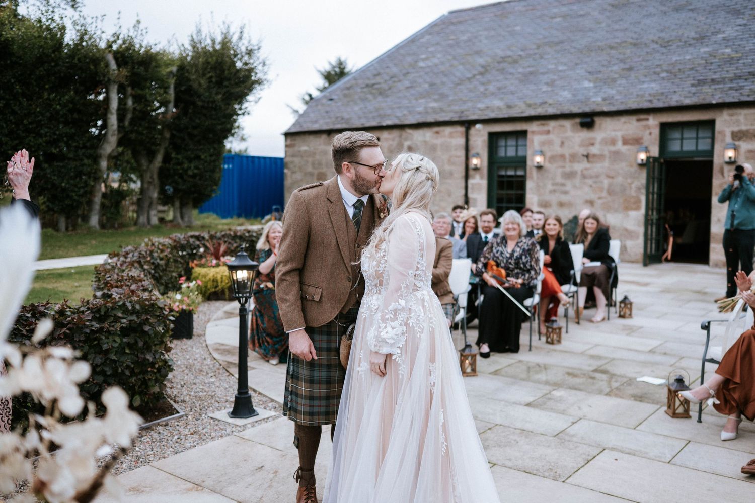 Stone building serves as rustic wedding venue with guests mingling on outdoor patio.
