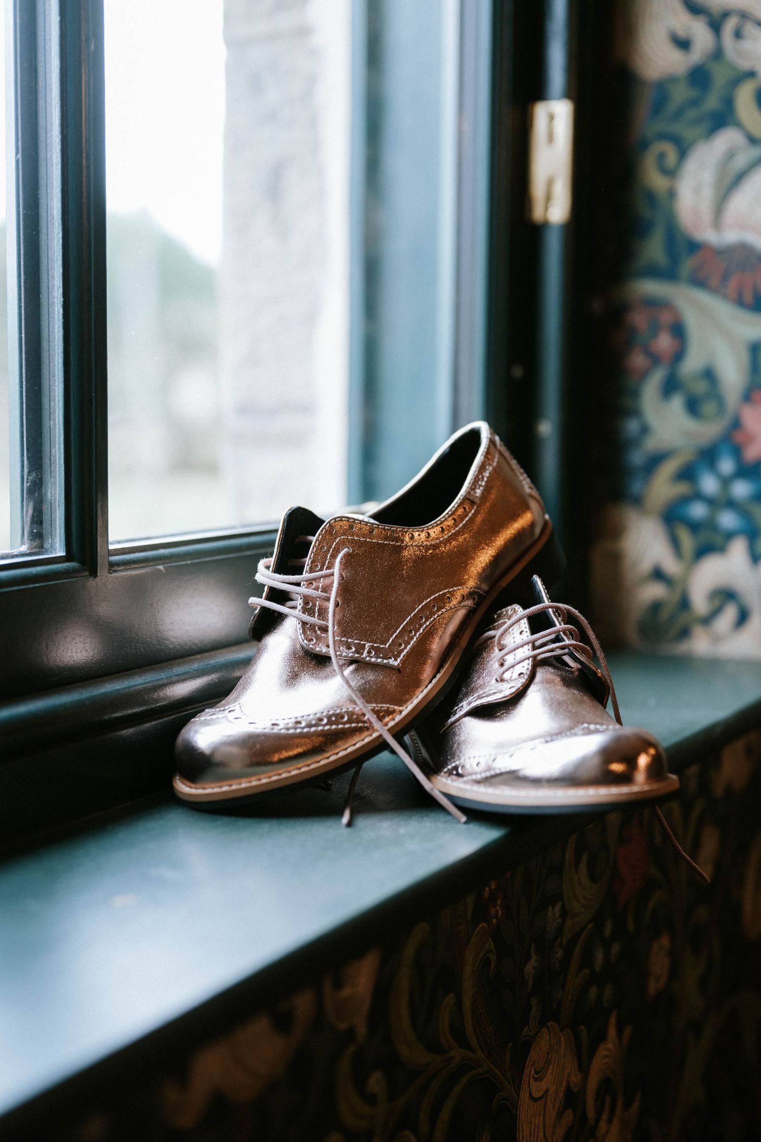 Brown leather dress shoes displayed on a windowsill in natural light.