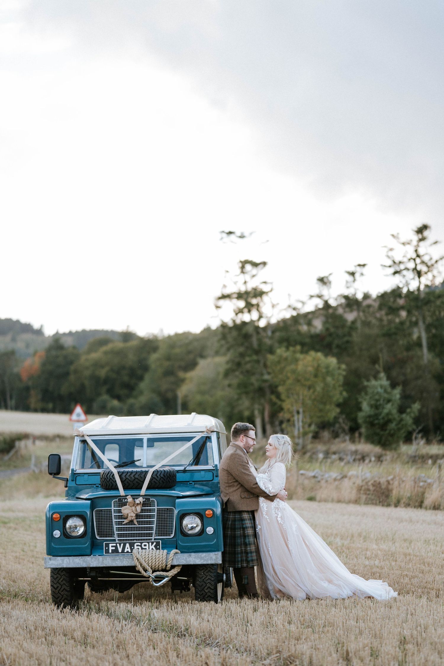 Vintage blue car parked in rustic field setting for wedding photography.