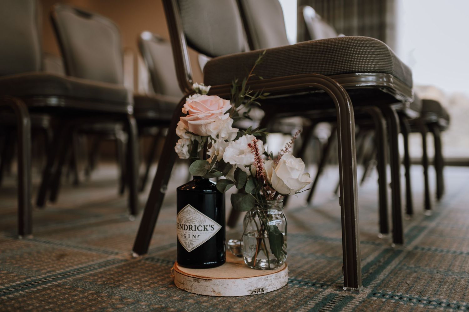 Mason jar flower arrangements with pink roses decorate chairs along a carpeted aisle.
