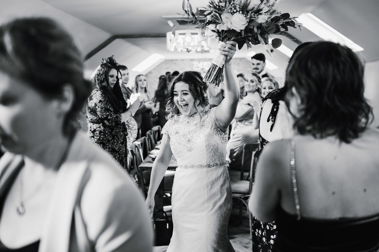 Black and white photo captures celebratory moment at indoor wedding reception.