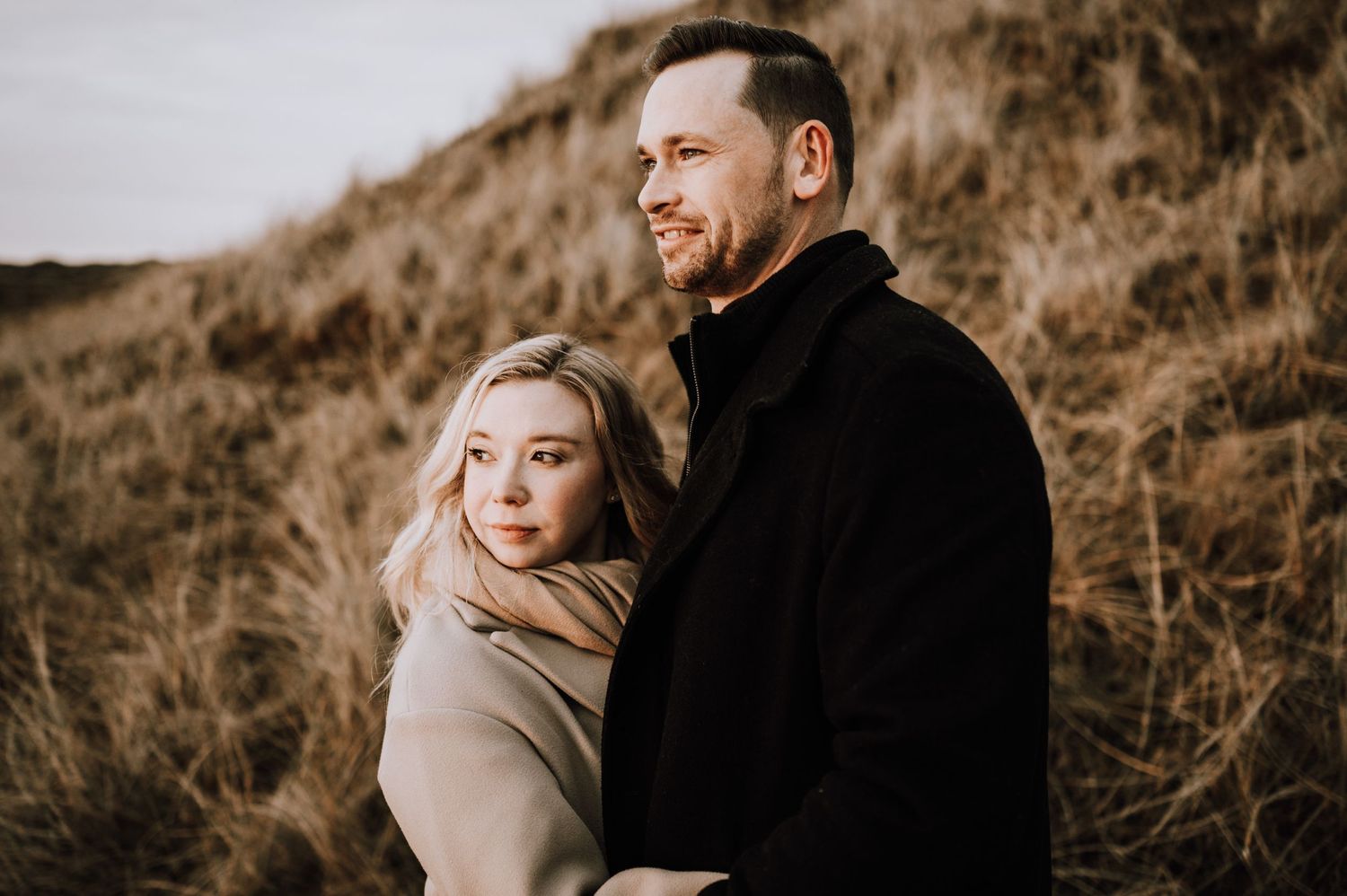 Romantic couple poses on coastal clifftop during moody winter photoshoot.