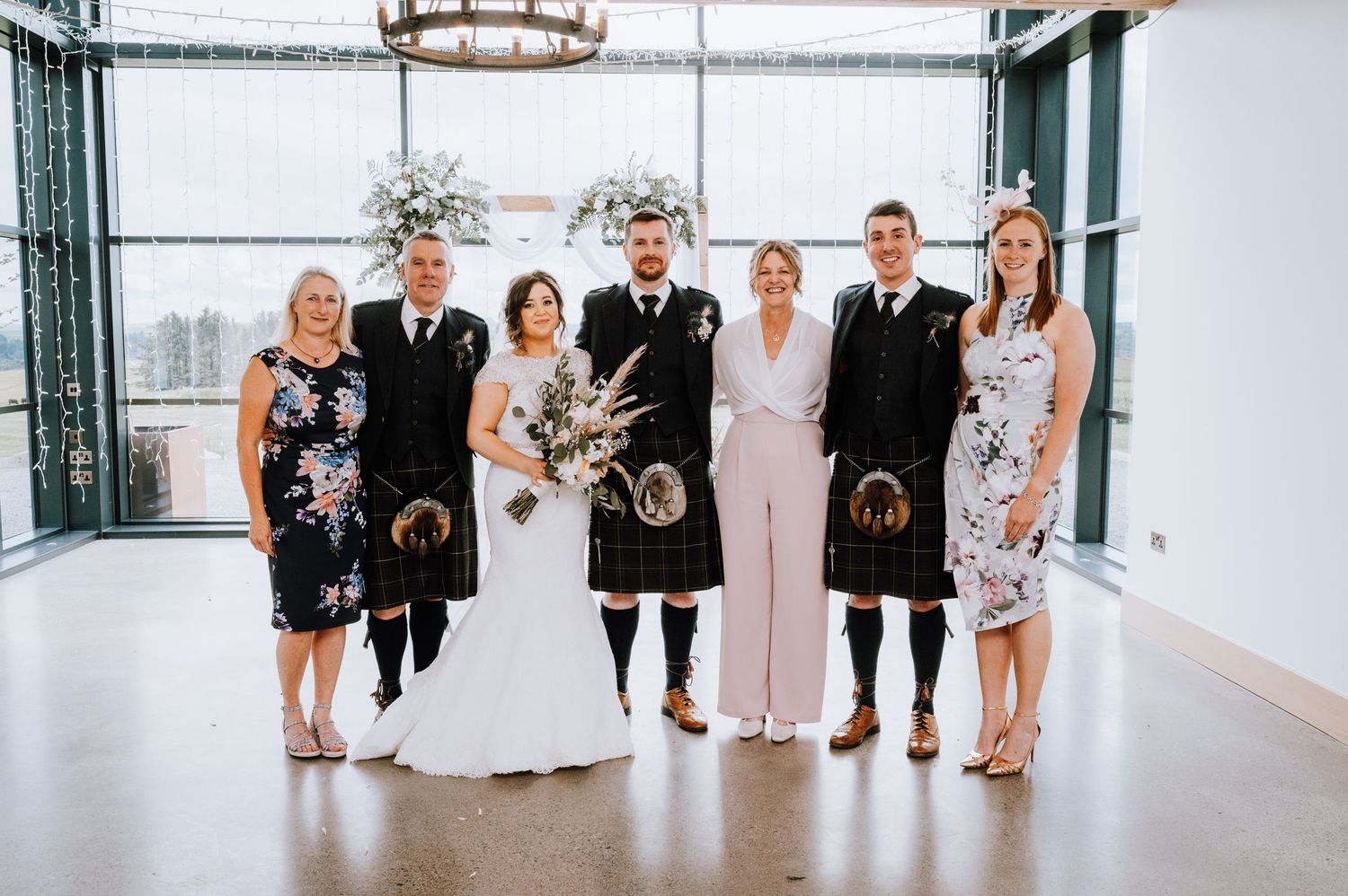 Formal wedding party portrait in modern venue with Scottish kilts and elegant attire.