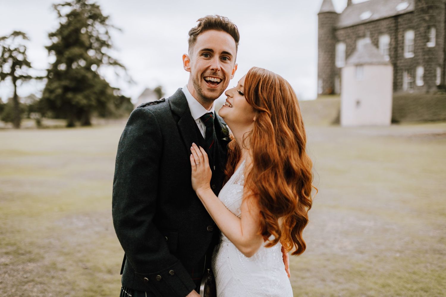 A wedding couple shares a joyful candid moment together on castle grounds in Scotland.