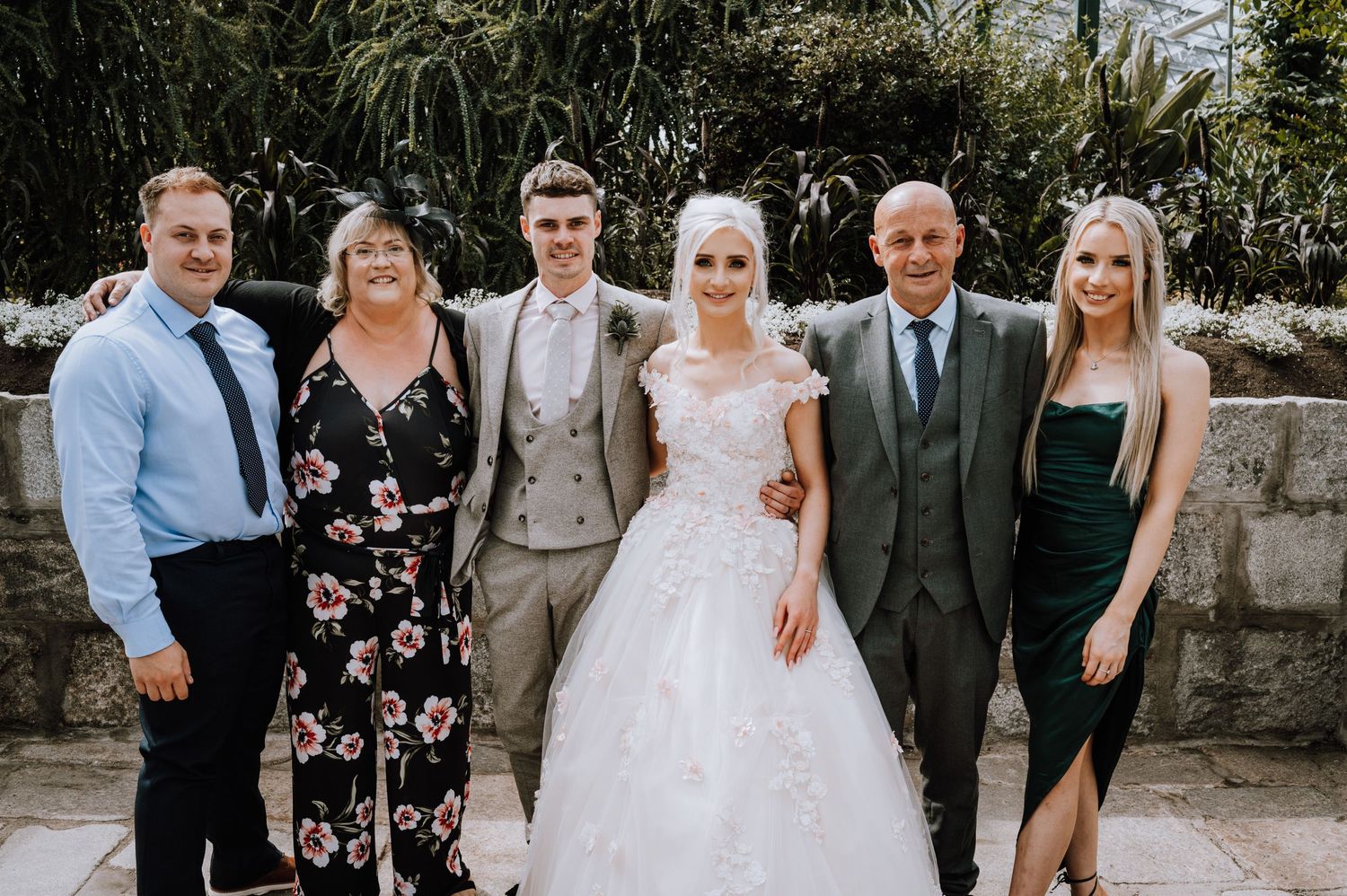 A small wedding group poses outdoors in formal attire.