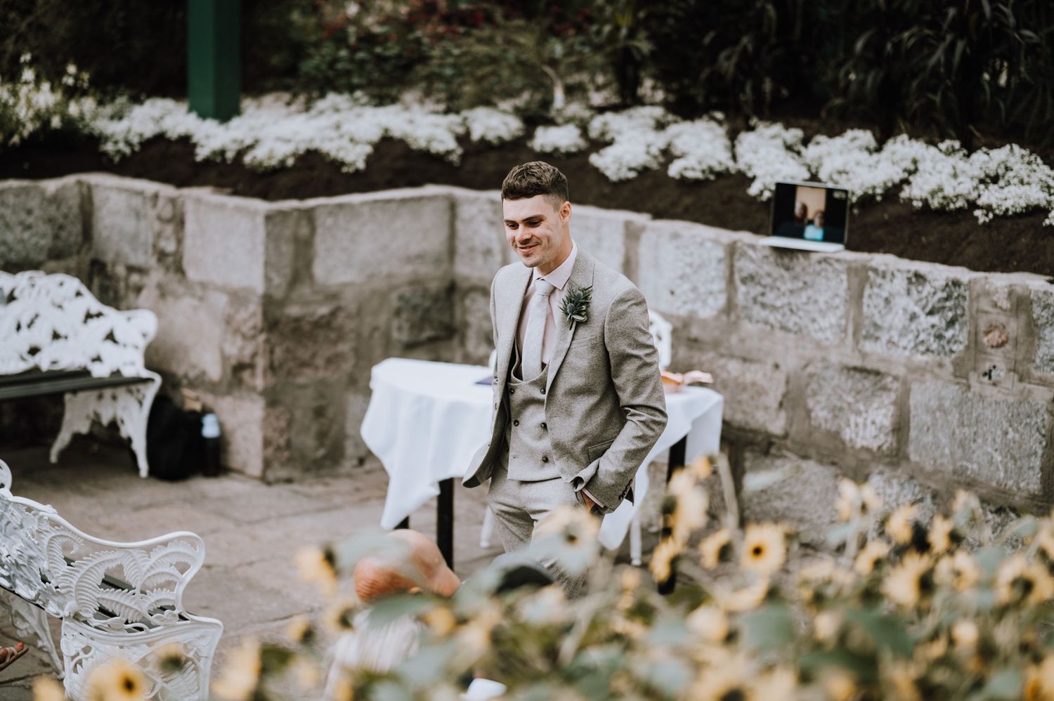 Wedding reception setting outdoors with stone walls and white floral decorations.
